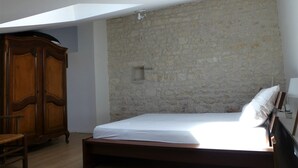 Quarto com parede de pedra, cama de madeira, guarda-roupa de madeira e uma pequena janela.