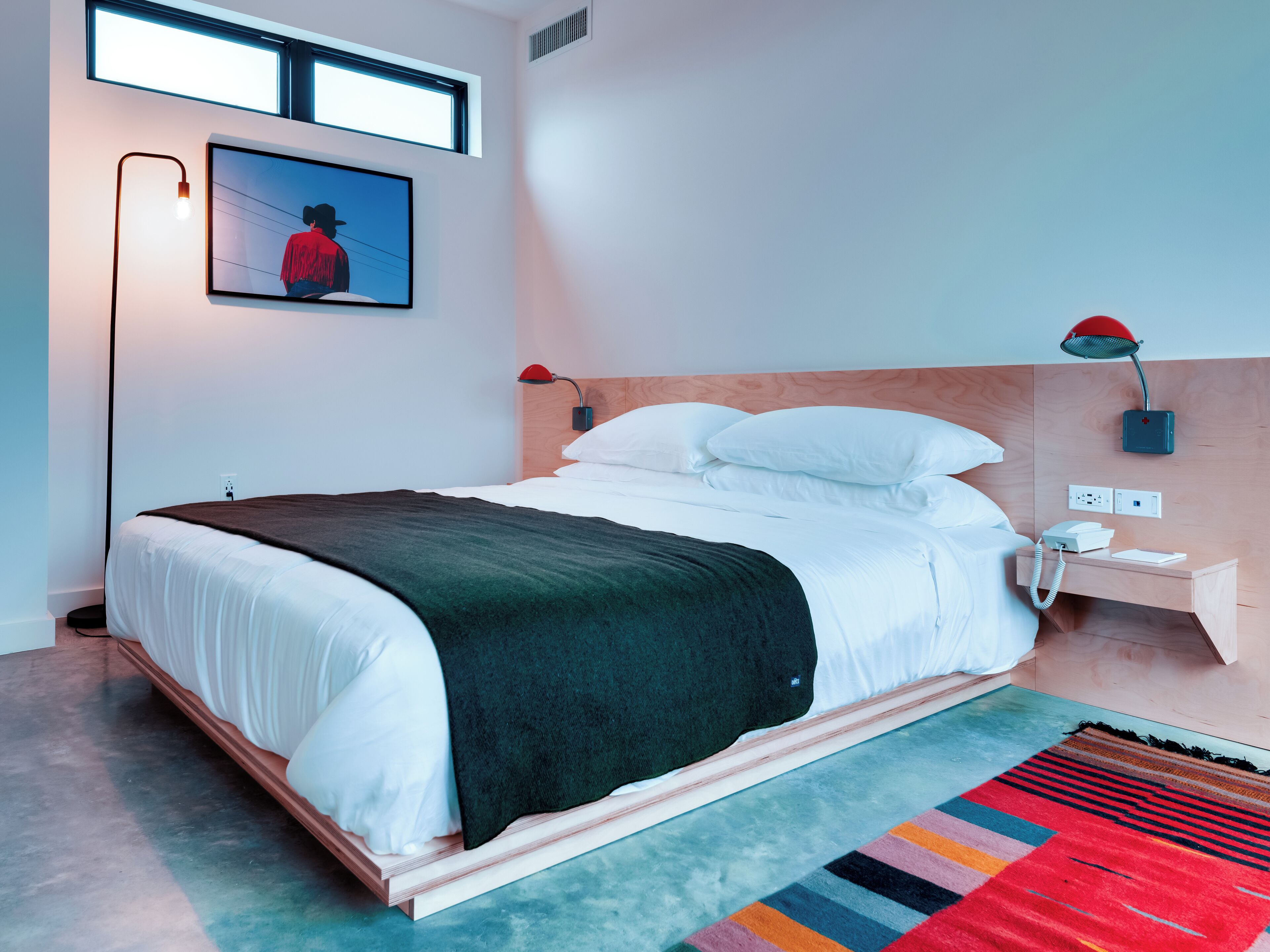 A modern hotel room with a bed, bedside table, lamp, and a framed picture on the wall.