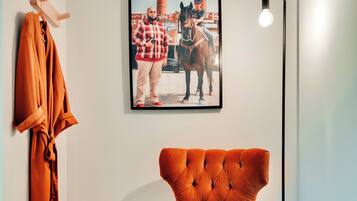 A room with a tufted orange armchair, a framed photograph on the wall, and a floor lamp.