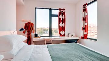 Una habitación de hotel con cama, escritorio y ventana con cortinas.