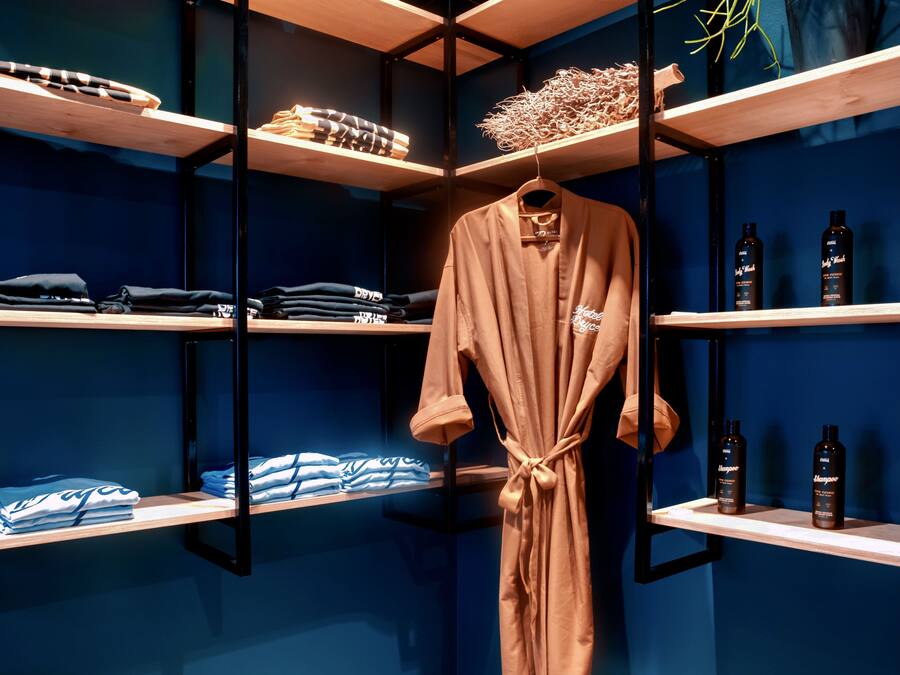 Een hotelkamer met een blauwe muur, houten planken met opgevouwen kleding en een badjas aan een rek.