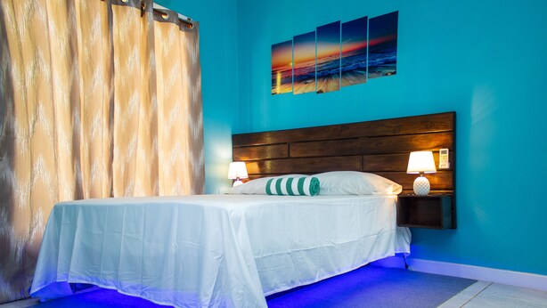 A neatly made bed with white linens, a wooden headboard, and two bedside lamps. - Near the beach family (West End)