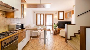 Eine kompakte Küche mit Gasherd, Mikrowelle und Holzschränken. Es gibt einen Essbereich mit Tisch und Stühlen sowie eine Treppe, die zu einer weiteren Ebene führt.
