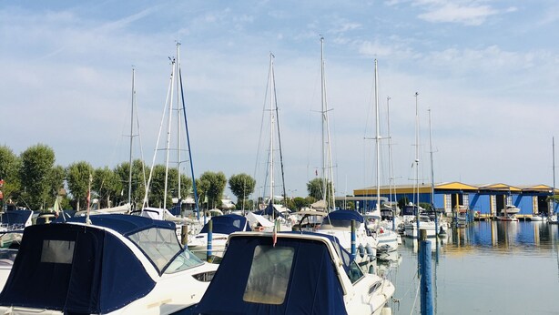 Ein Yachthafen mit mehreren angestuften Booten, einer Holzsteganlage und einem Gebäude mit blauem Dach im Hintergrund.