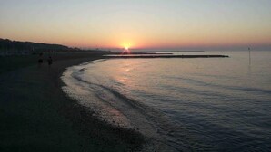 Ein Sonnenuntergang über einem ruhigen Meer mit einer geschwungenen Küstenlinie und einem Steg, der sich ins Wasser erstreckt.