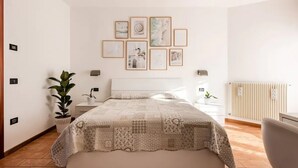 Ein Schlafzimmer mit Bett, Nachttischen, einem Heizkörper und gerahmten Bildern an der Wand.