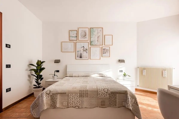 Ein Schlafzimmer mit Bett, Nachttischen, einem Heizkörper und gerahmten Bildern an der Wand.