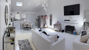 A modern living room with a white sofa, a dining area, and a kitchen. - Cozy Hamptons Escape 3BR Minutes From Beach! (Hampton Bays)