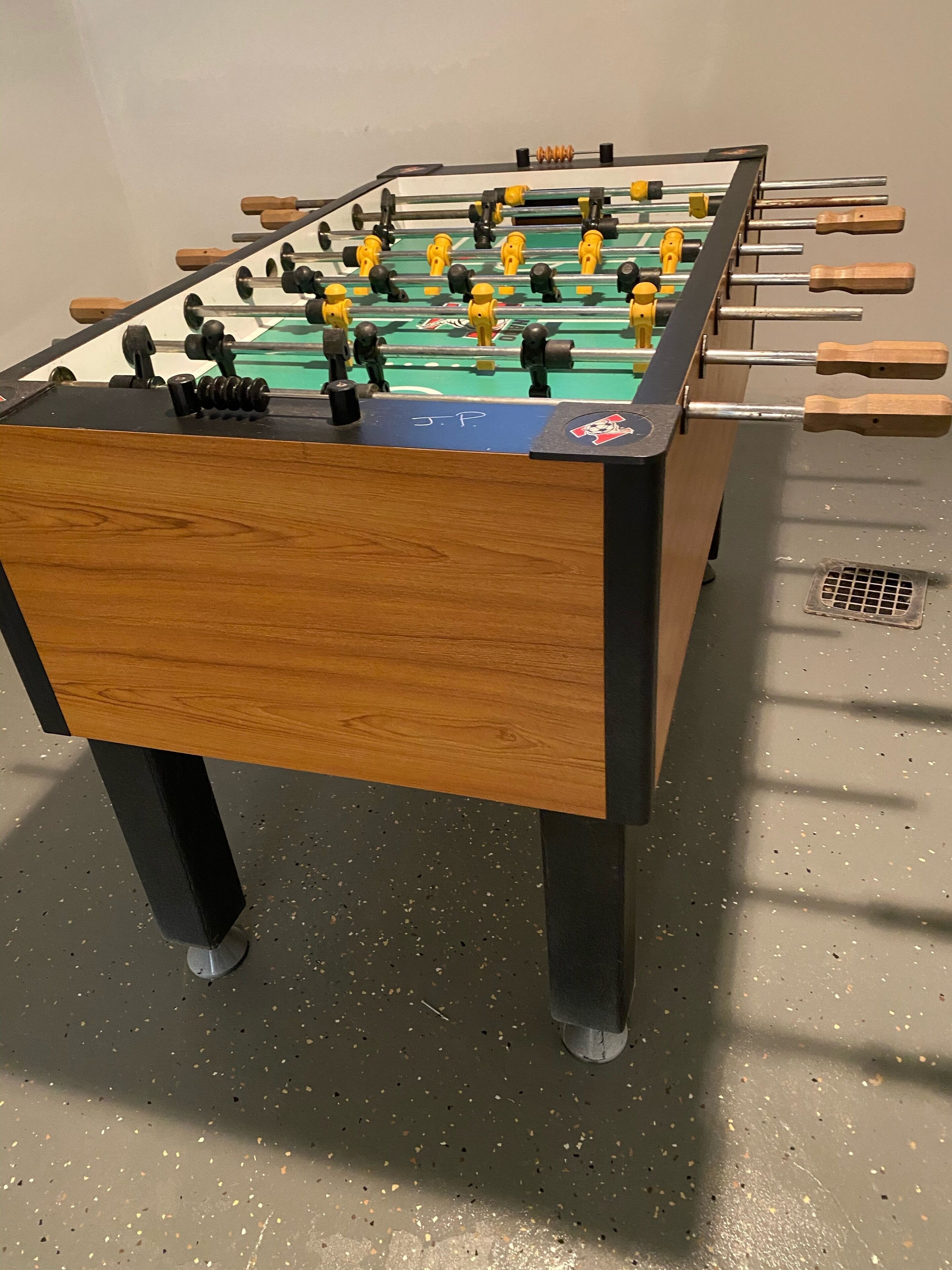 Une table de baby-foot en bois, avec un plateau de jeu vert et des figurines noires et jaunes.