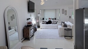 A modern living room with a checkered floor, a large mirror, a sofa set, a dining table with a white tablecloth, and a kitchen area with a refrigerator. - Cozy Hamptons Escape 3BR Minutes From Beach! (Hampton Bays)