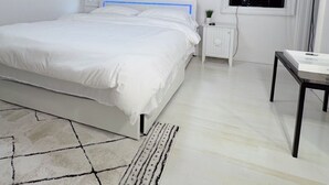 A modern bedroom with a large bed, a bedside table, a TV, and artwork on the walls. - Cozy Hamptons Escape 3BR Minutes From Beach! (Hampton Bays)