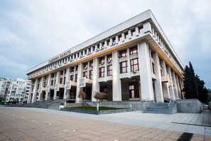 Un grand bâtiment moderne à la façade symétrique, doté de nombreuses fenêtres et d’une entrée centrale avec des marches.