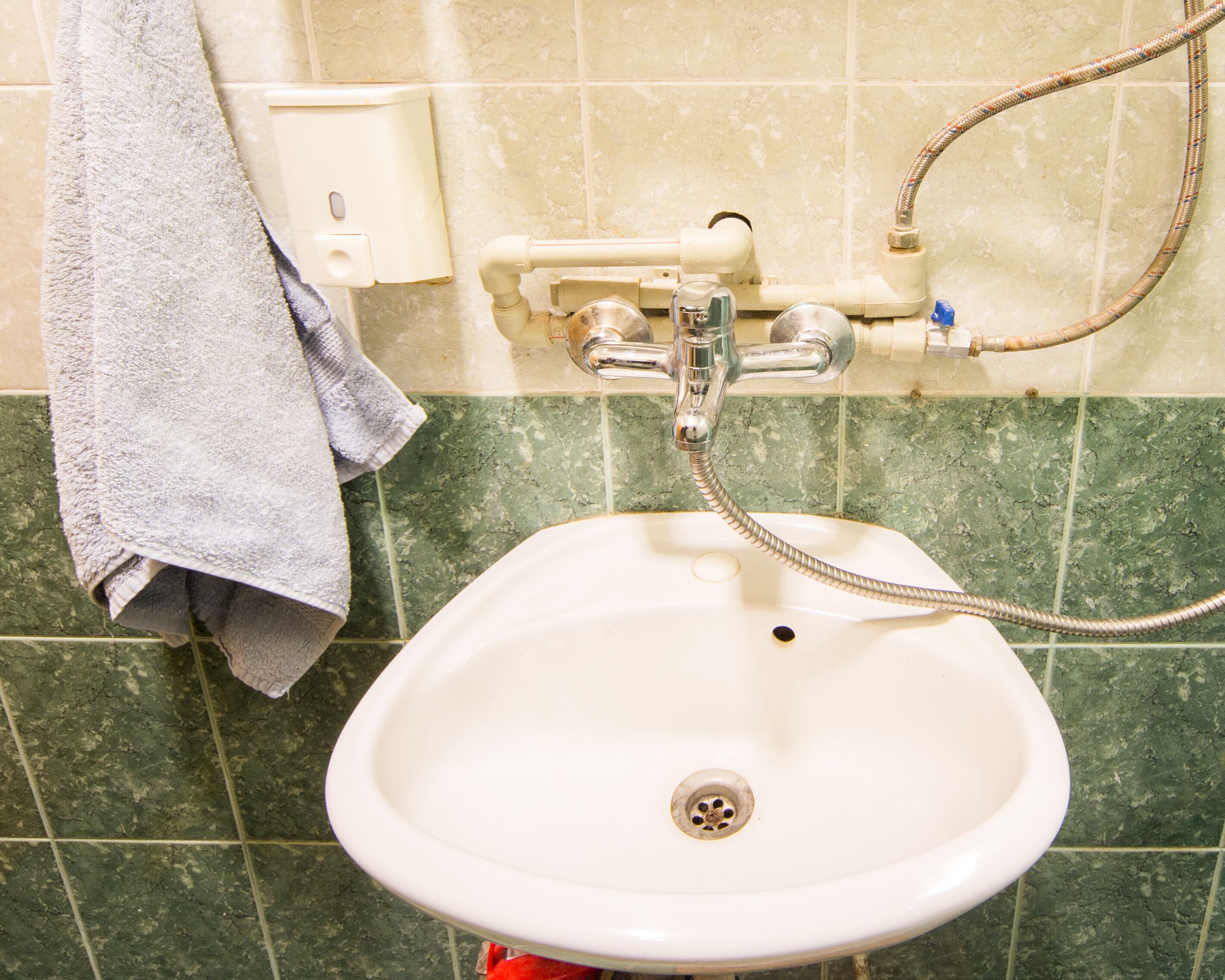 A bathroom sink with a handheld showerhead, a towel hanging on the wall, and a soap dispenser.