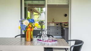 Ein Essbereich mit einem Tisch für vier Personen, einer Blumenvase und einer durchgehenden Tür einsehbarer Küche.