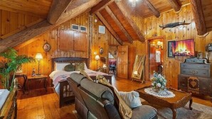 Interior d'una cabana de fusta amb un dormitori a la llotja, una zona de seients amb un sofà i una taula de centre, i una llar de foc.