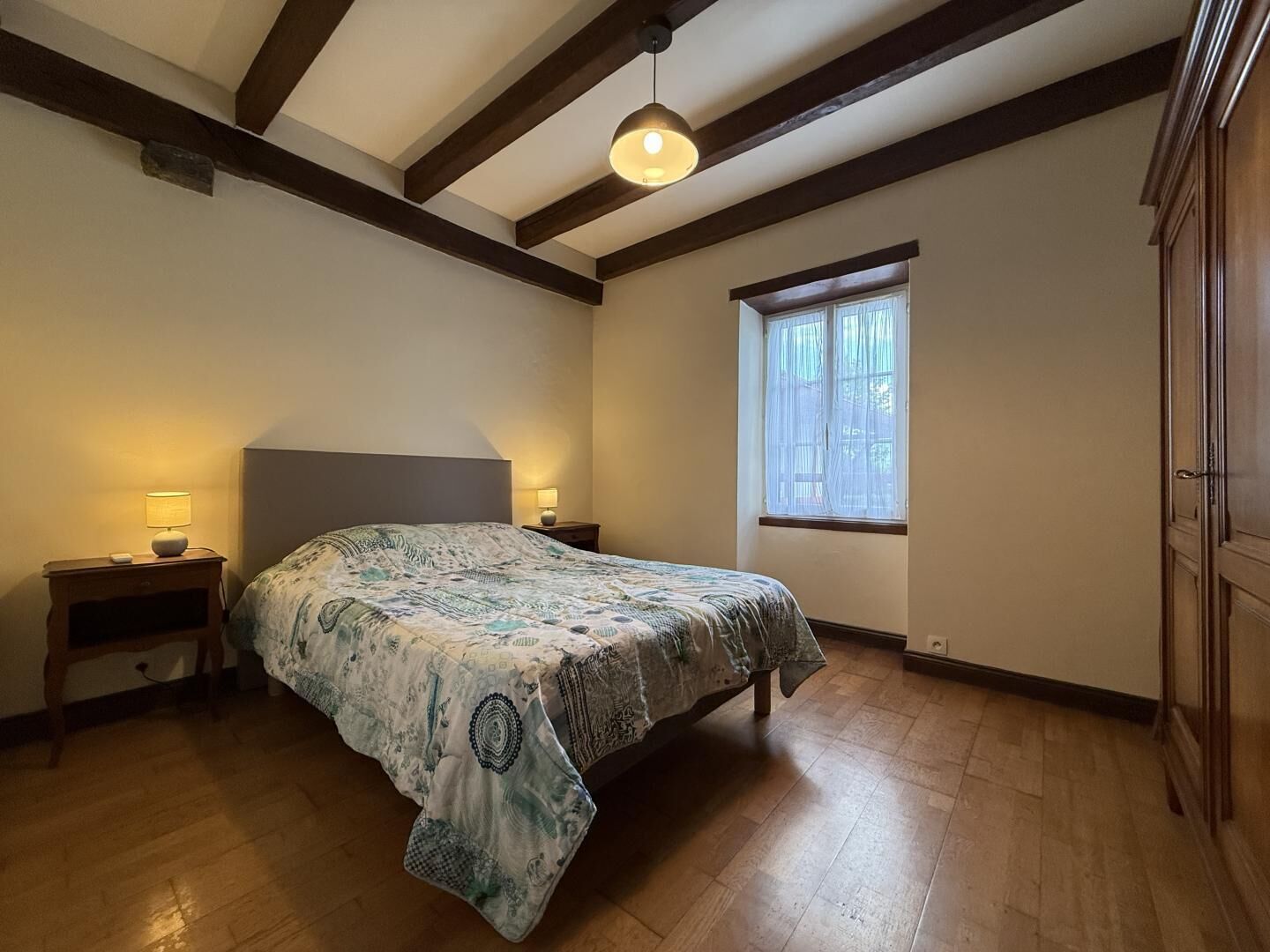 Une chambre à coucher avec un lit, deux lampes de chevet, une fenêtre et des poutres en bois au plafond.