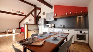 Eine moderne Küche mit Essbereich, mit einem Holztisch, der mit Tassen mit Sternmuster dekoriert ist, einer roten Akzentwand und einem Deckenventilator.