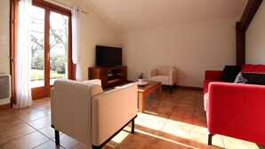 Ein Wohnzimmer mit Fernseher, einem roten Sofa, einem beigen Sessel und einem Holztisch.