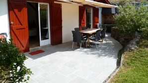 Ein Haus mit einer Terrassenfläche, die einen Tisch und Stühle, eine Schiebetür und eine rote Tür zeigt.