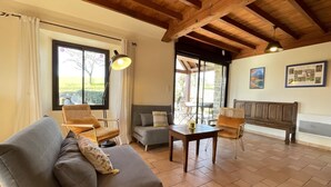 Amplia sala de estar con un sofá gris, un banco de madera y una mesita. Ventanas grandes permiten la entrada de luz natural y vistas al exterior.