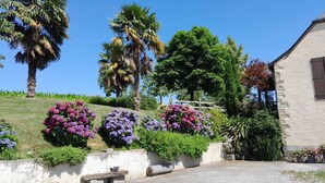 Una zona residencial con una casa, una colina cubierta de césped y diversas plantas en flor.