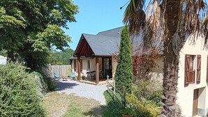 Una casa con porche techado, camino de entrada de grava y vegetación circundante.