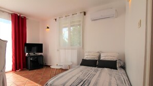 A bedroom with a bed, a TV, a small table, and a window with curtains.