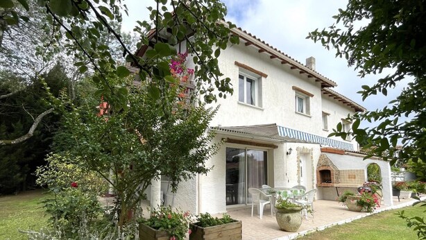A two-story house with a patio, a stone oven, and a garden with potted plants.