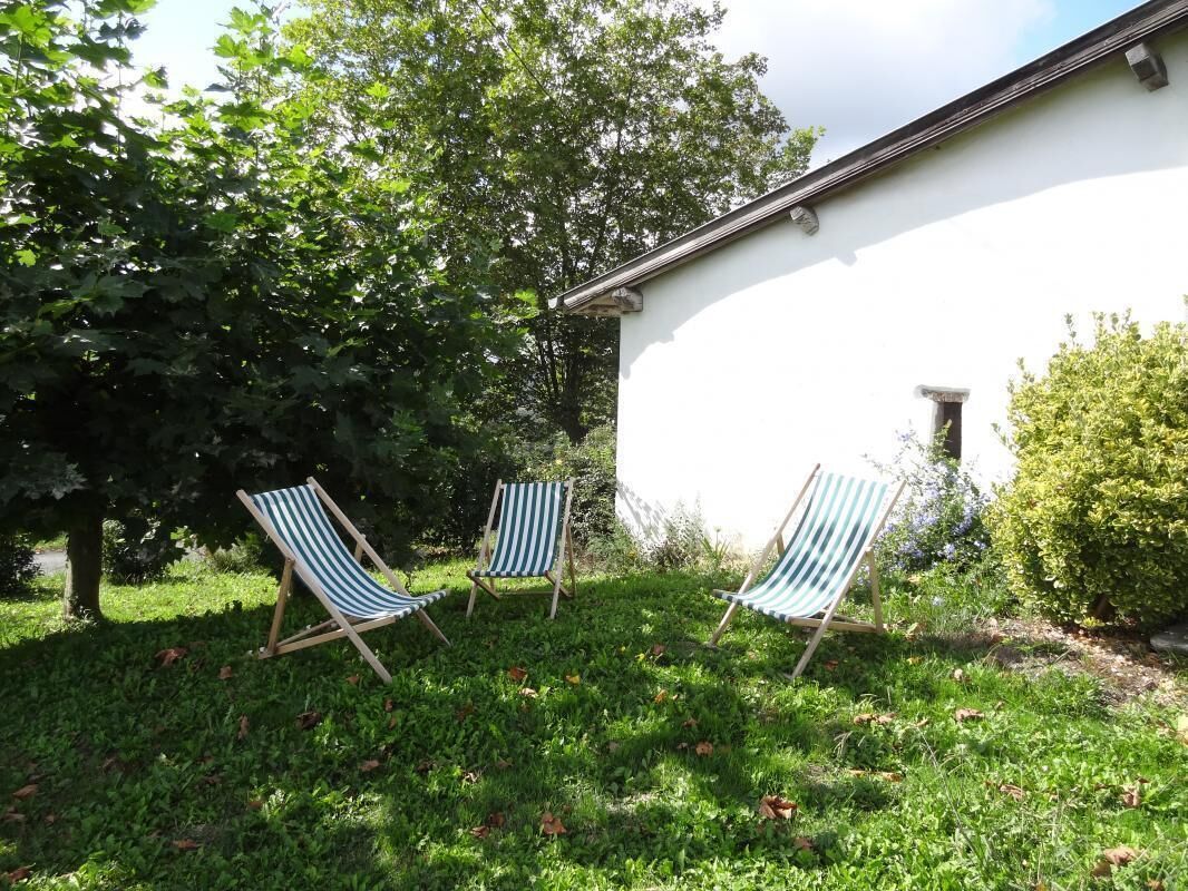 A white building with a sloped roof and a small window. There are two striped lawn chairs in front of the building.