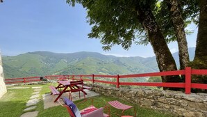 Ein Picknickplatz mit einer Steinsäule, rotem Zaun und Blick auf grüne Hügel.