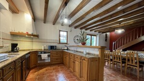 A spacious kitchen with wooden cabinets, a large island, and a dining area with wooden chairs and a table. - Aikobeko - Sare - Gîte (SARE)