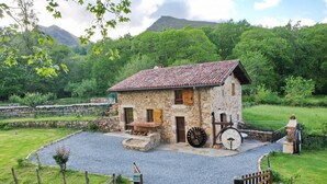 Une maison en pierre avec un toit de tuiles, une grande roue et une allée gravillonnée.
