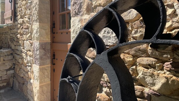 Un bâtiment en pierre avec une porte en bois et de grandes roues en métal fixées au mur.