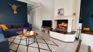 Een woonkamer met een blauwe bank, een salontafel met een theepot, een open haard en een televisie.