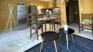 Espaço compacto com cozinha compacta, área de refeições com mesa redonda e cadeiras, aquecedor portátil e pequena área de estar com uma poltrona e sofá.