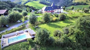 Uma casa grande com piscina, cercada por vegetação exuberante e colinas ondulantes ao fundo.
