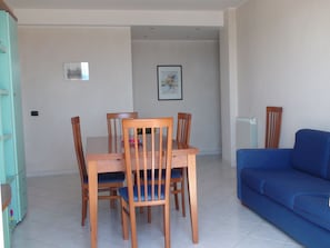 Un coin repas avec une table et des chaises en bois, un canapé bleu et un espace cuisine avec des placards.