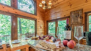 Interior de una cabaña de madera con una mesa de comedor dispuesta para una comida, mostrando una variedad de quesos, carnes y frutas.