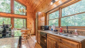 Interior de una cabaña de madera con cocina, comedor y ventanas amplias.