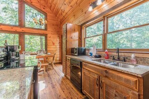 A wooden cabin interior with a kitchen, dining area, and large windows.