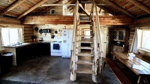 Ein rustikales Blockhaus-Interieur mit einer Holztreppe, einer Küchenzeile und einem Esstisch.