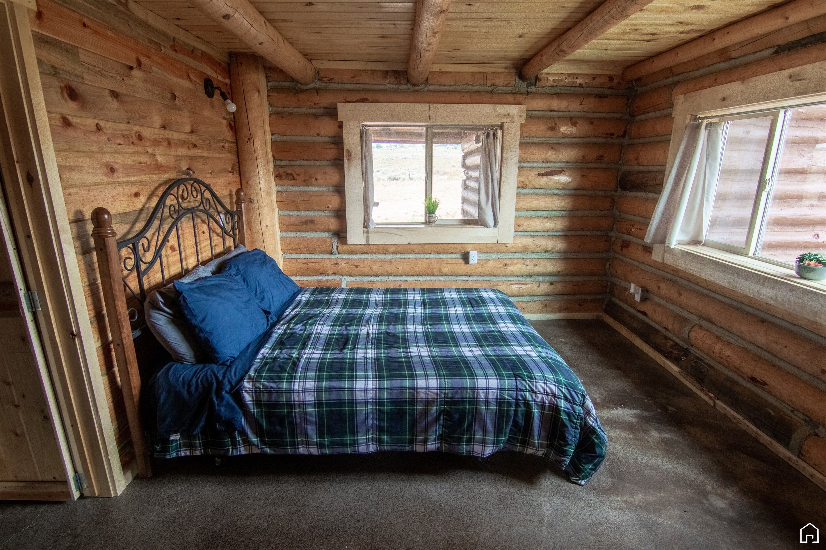 Une pièce de style cabane en bois, avec un lit, une fenêtre avec des rideaux et une petite plante posée sur le rebord de la fenêtre.