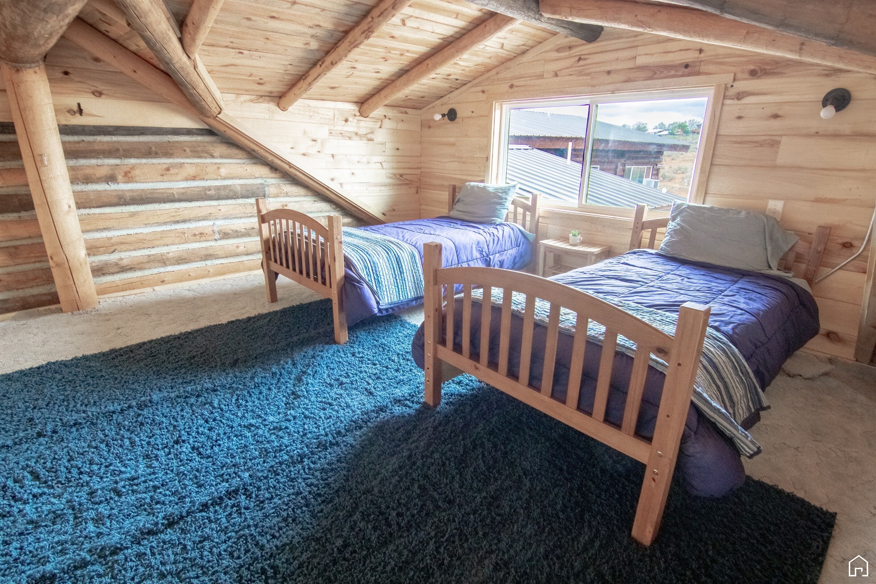 Un dormitorio acogedor en el ático, con techo inclinado, paredes de madera y un gran ventanal.