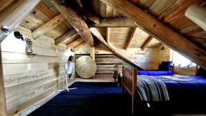 Ein gemütliches Schlafzimmer unter dem Dach mit Holzbalkendecke, einem großen runden Spiegel, einem Bett mit blauer Bettdecke und einem dunkelblauen Teppich.
