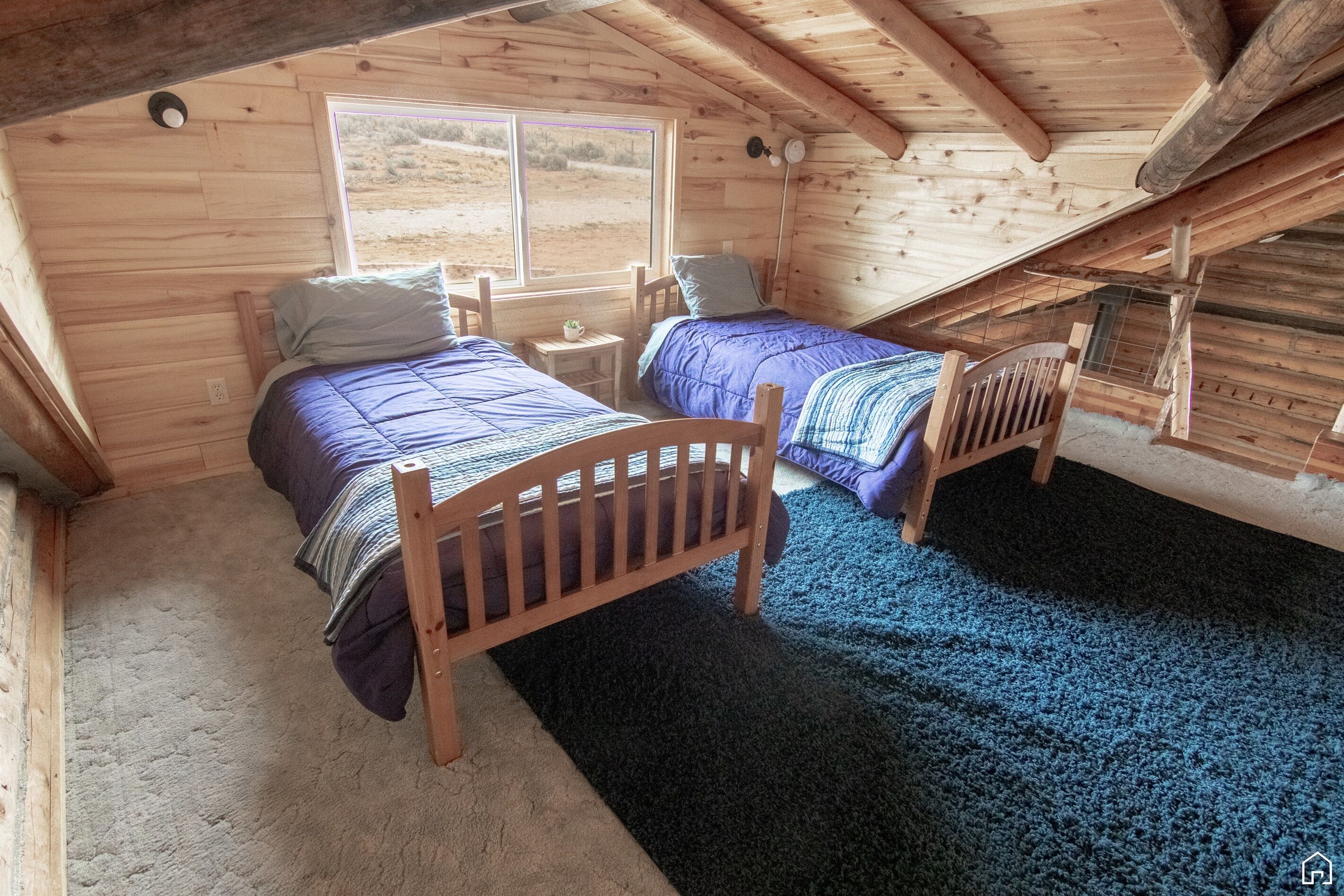 Ein gemütliches Schlafzimmer im Dachgeschoss mit zwei Holzbett, einem kleinen Tisch und einem Fenster mit Blick ins Freie.
