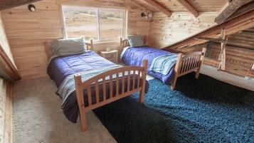 Ein gemütliches Schlafzimmer im Dachgeschoss mit zwei Holzbett, einem kleinen Tisch und einem Fenster mit Blick ins Freie.