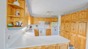 A kitchen with wooden cabinets, a white countertop, a stove, a microwave, and a refrigerator. - Coby’s Cove - Four Season Cottage Huntsville Muskoka Waterfront  (Emsdale)