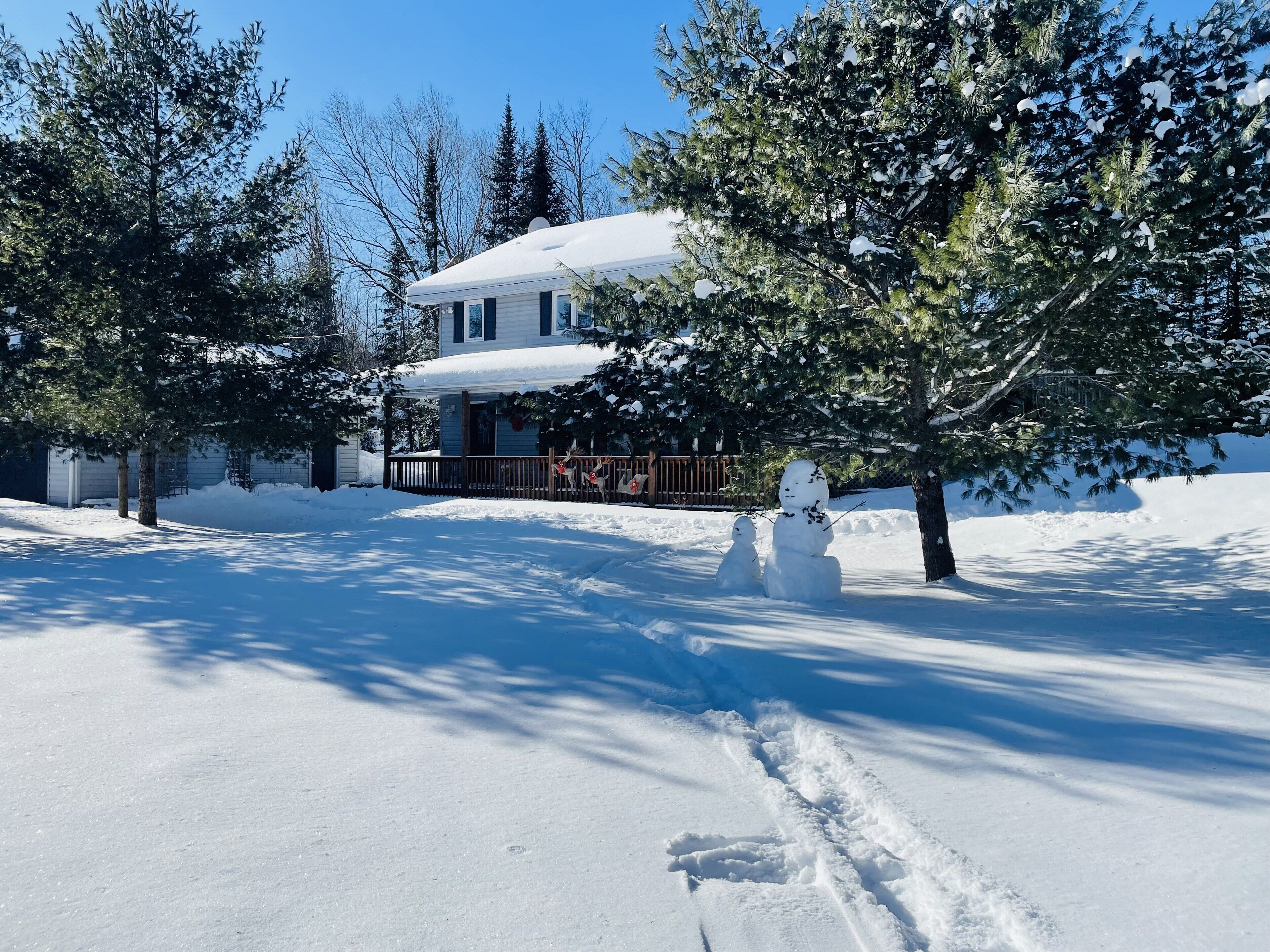 A snow-covered landscape with a house, trees, and a snowman.