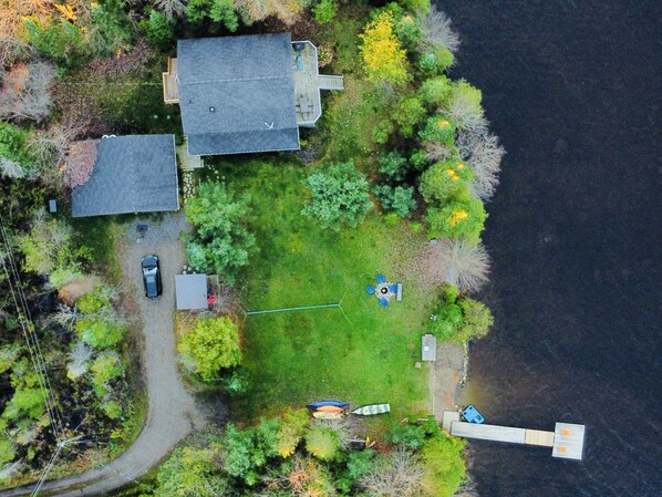 An aerial view of a residential area with a house, a driveway, a lawn, and a dock by a body of water.