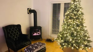 A cozy living room with a black leather armchair, a small ottoman, a wooden floor, a Christmas tree, and a wood-burning stove. - Coby’s Cove - Four Season Cottage Huntsville Muskoka Waterfront  (Emsdale)